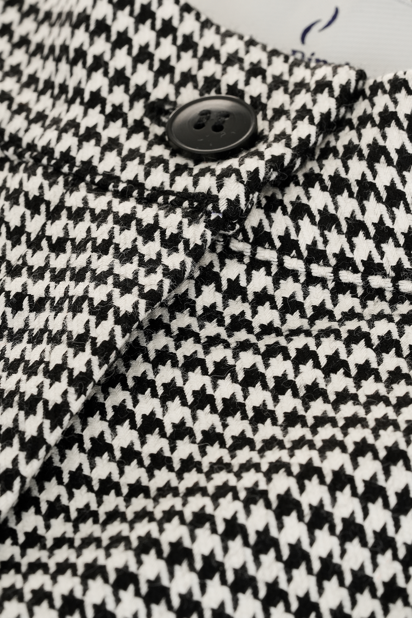 Close-up of a houndstooth patterned fabric coat with a black button showcasing classic and elegant fashion style suitable for various formal and casual occasions.