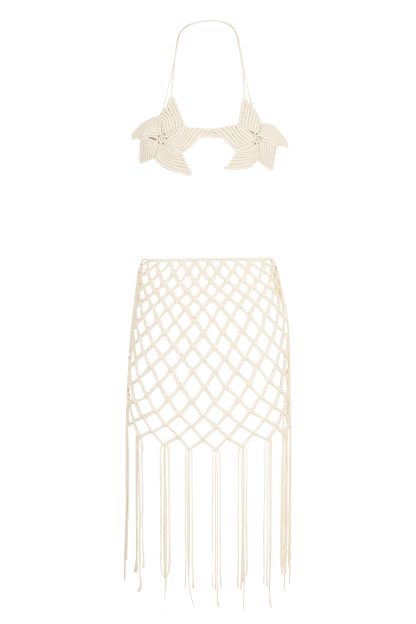 This image showcases a two-piece macramé set in an off-white color. The top is a starfish-shaped bustier with thin straps and a detailed woven design, accented by a pearl in the center of each starfish. The bottom piece is a skirt with an intricate lattice-like weave, ending in long, fringed tassels. The set exudes a coastal, bohemian charm, perfect for summer events or beachwear.