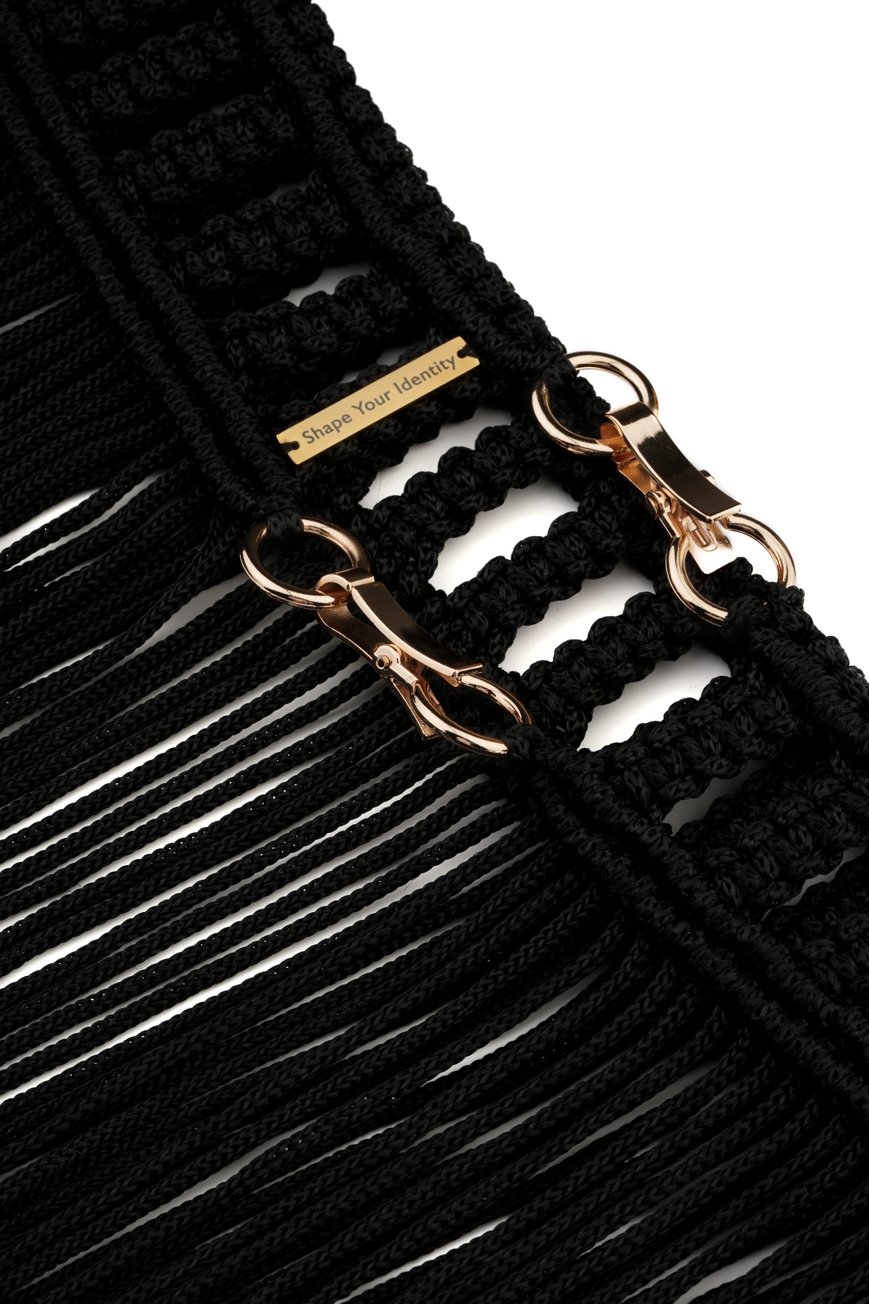 Close-up of an elegant black macramé design with shiny gold clasps and a small engraved tag showcasing intricate craftsmanship and modern fashion details.